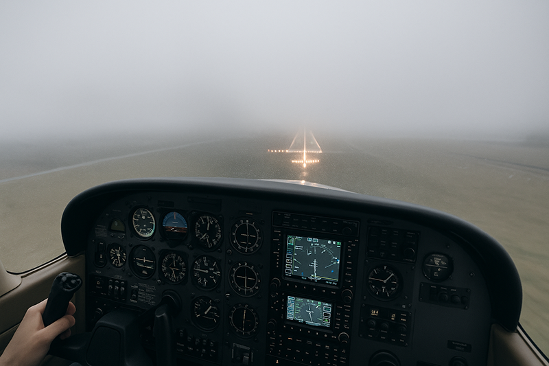 Instrument aircraft cockpit on final approach toward a runway under low clouds and reduced visibility
